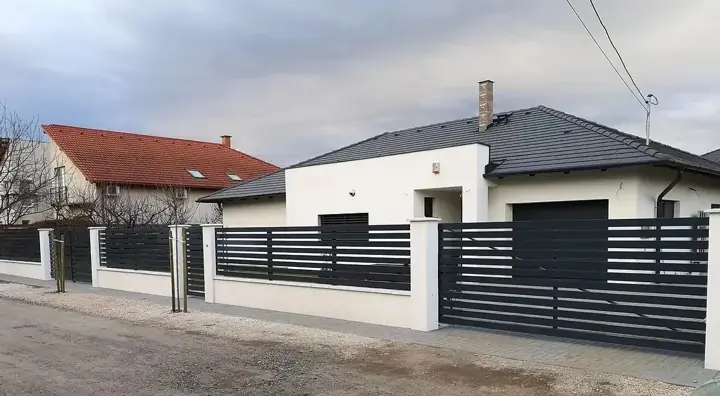 Fehérre vakolt zsalukő kerítés pillérekkel és antracit vízszintes léc mezőkkel modern ház előtt