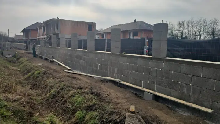 Hosszú zsalukő kerítésfal pillérekkel építés közben a telekhatáron
