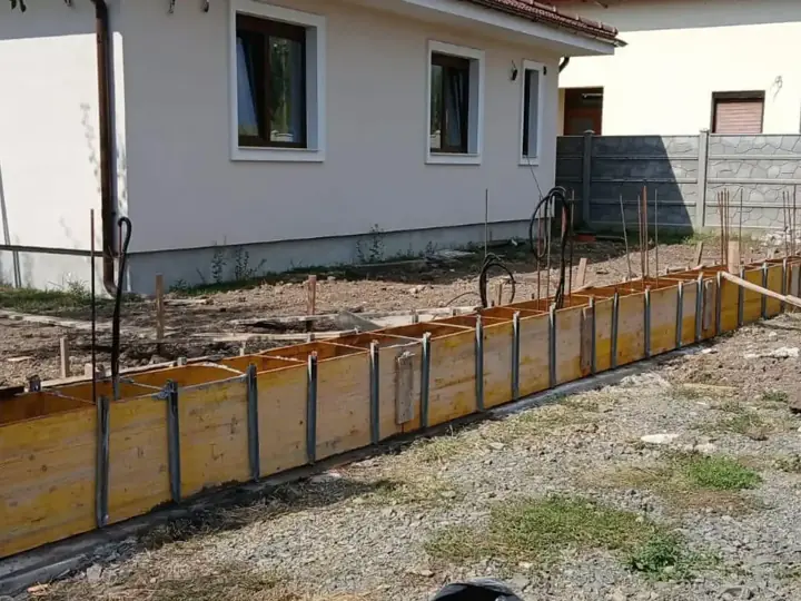Zsalukő kerítés sávalapjának fa zsaluzata vasszereléssel családi ház előtt